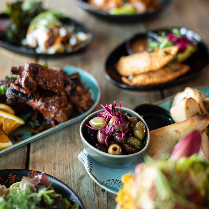 A sharing board of tapas: olives, ribs, empanadas and flatbread
