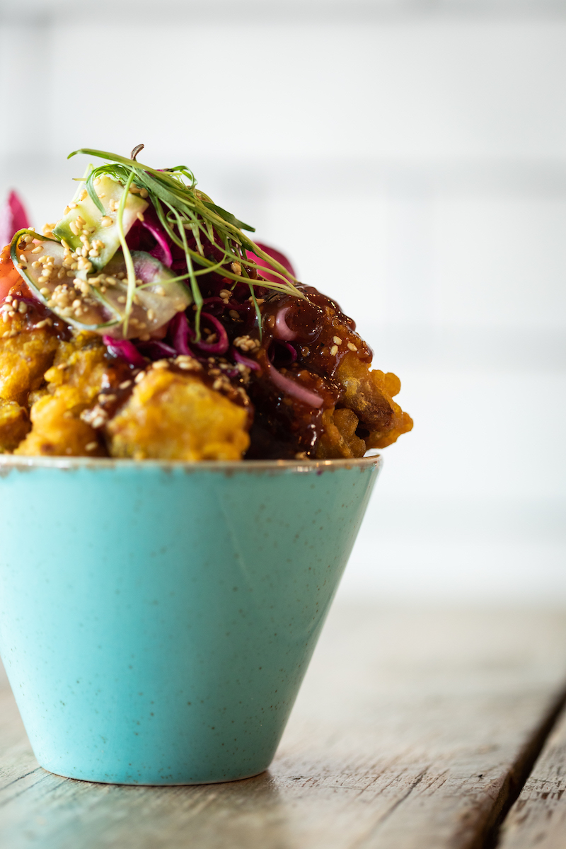 A bowl of crispy bites topped with pickles and sesame