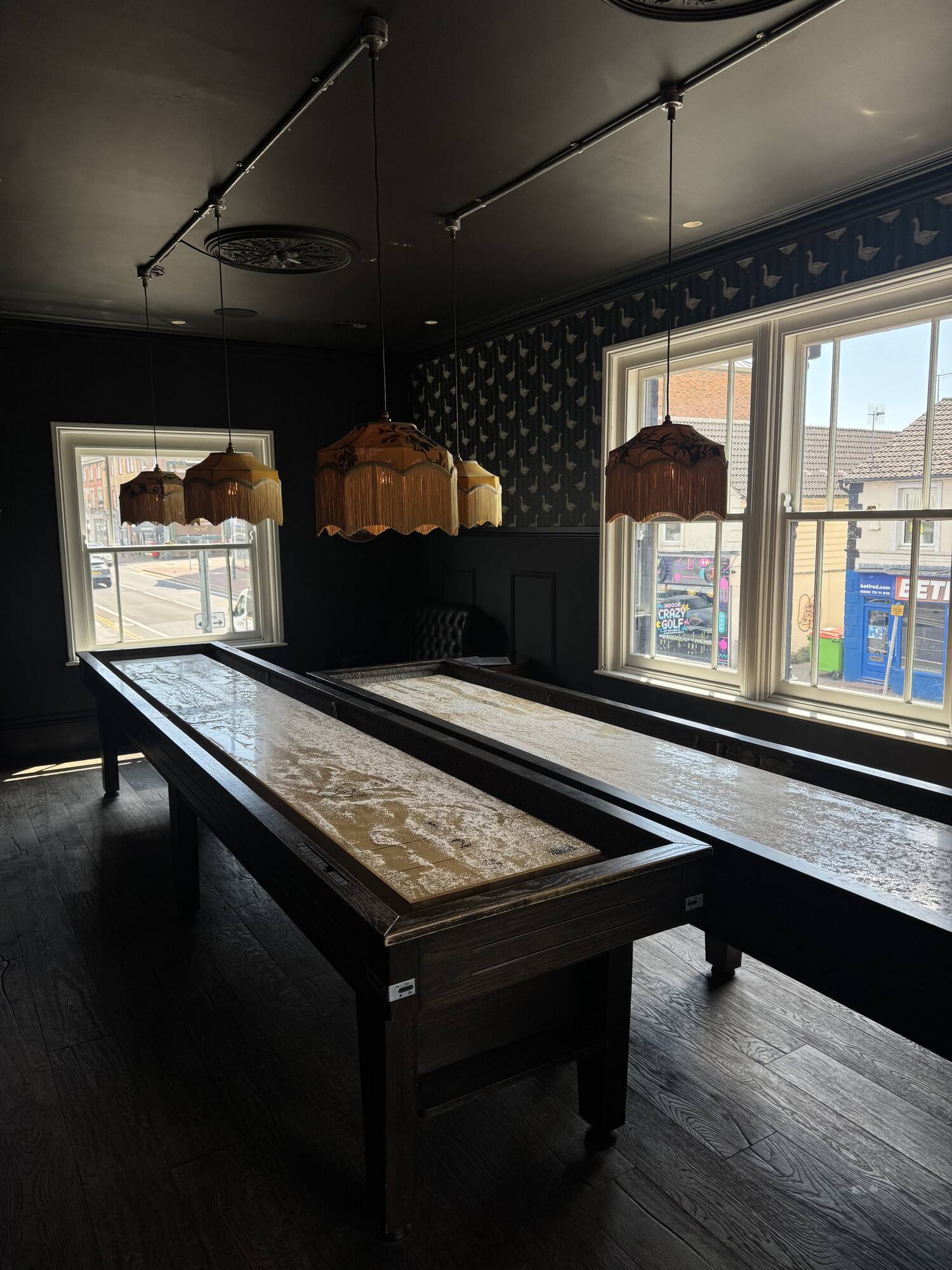 Two 14-foot shuffleboard tables side by side under fringed Tiffany lamps