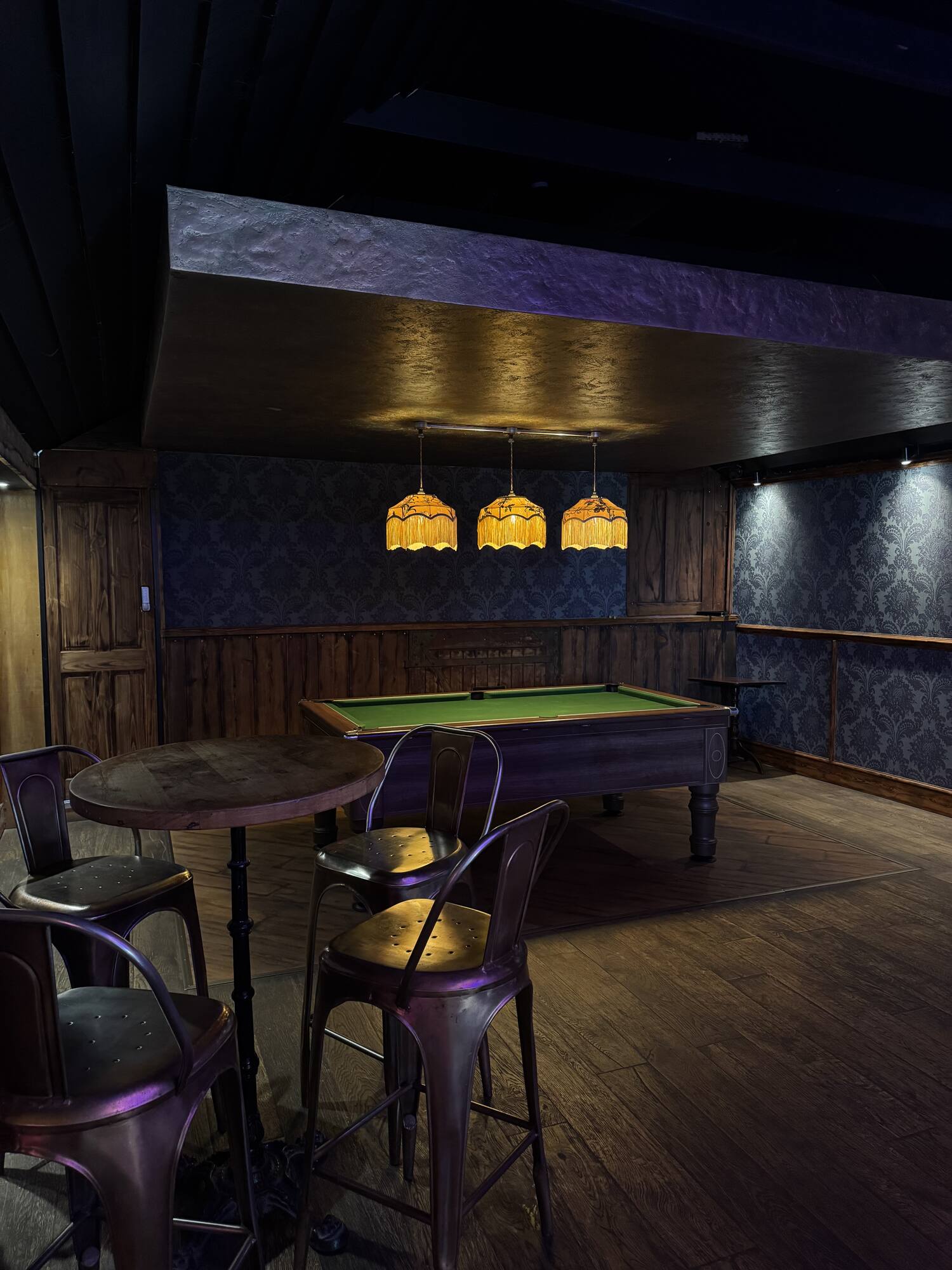 A cosy corner with a high table, bar stools and a pool table under patterned walls