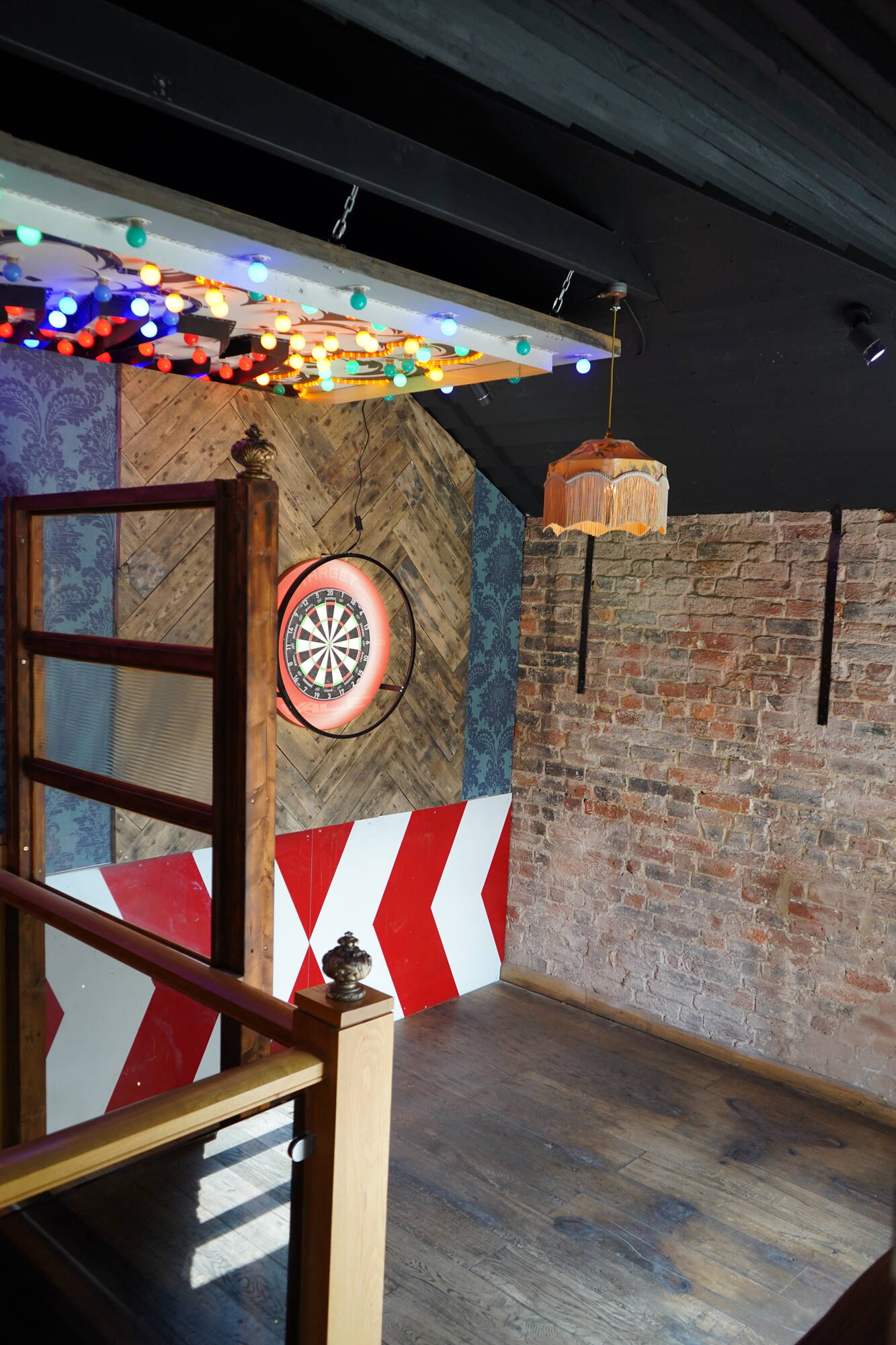 A traditional dartboard on exposed brick above a red and white chevron oche
