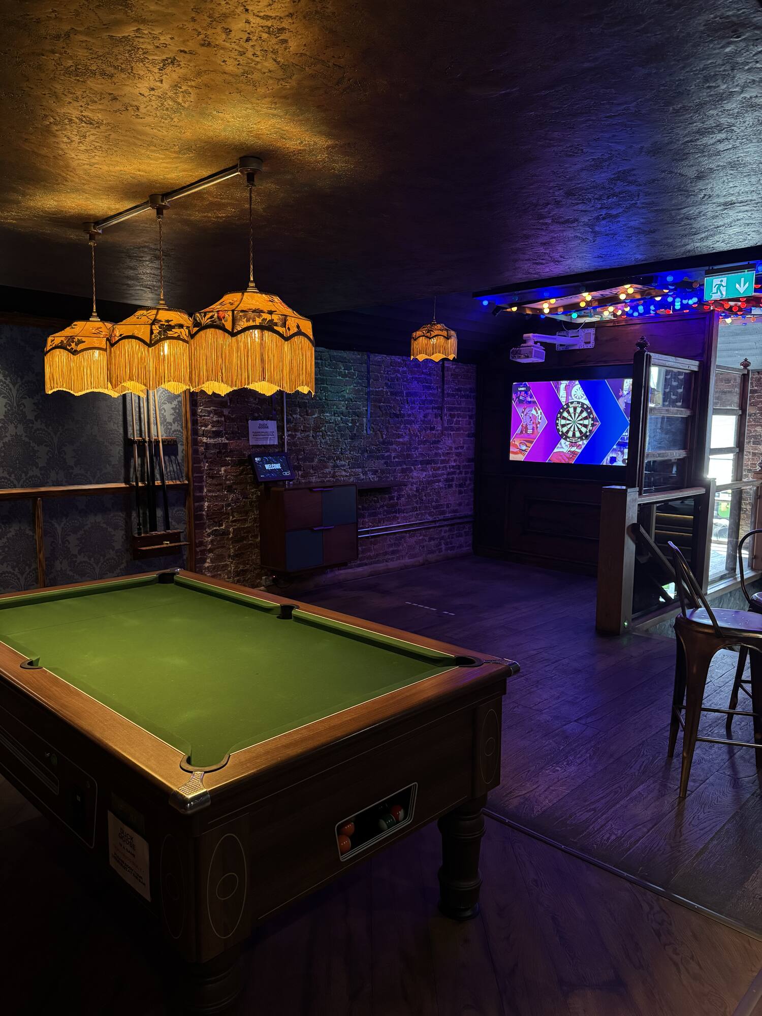 A pool table glowing under neon and fringed lamps at night
